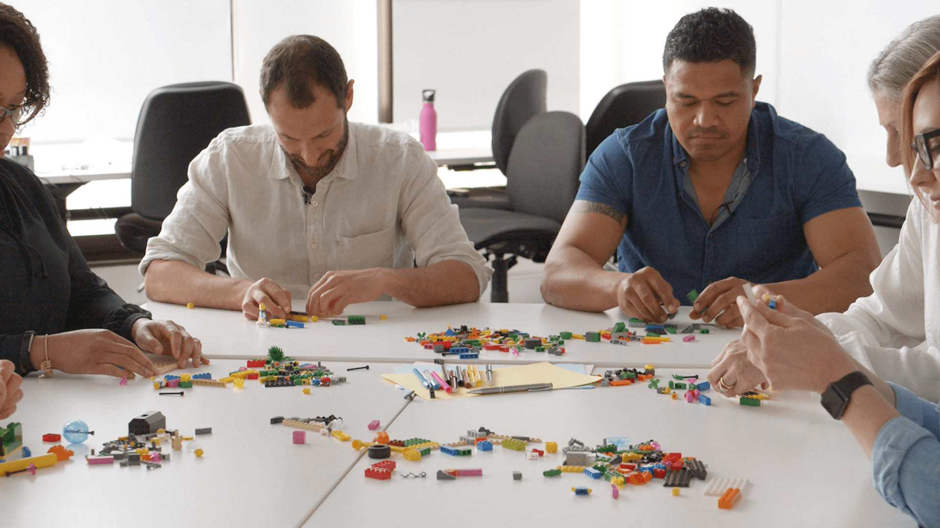 Team of 4–8 participants using colorful LEGO bricks in a design thinking workshop to build 3D models and align on creative solutions.